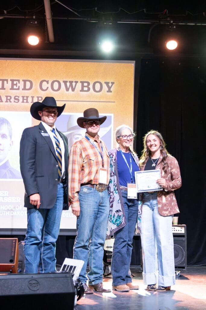 Four people on a stage posing with certificates at a Western-themed award event.