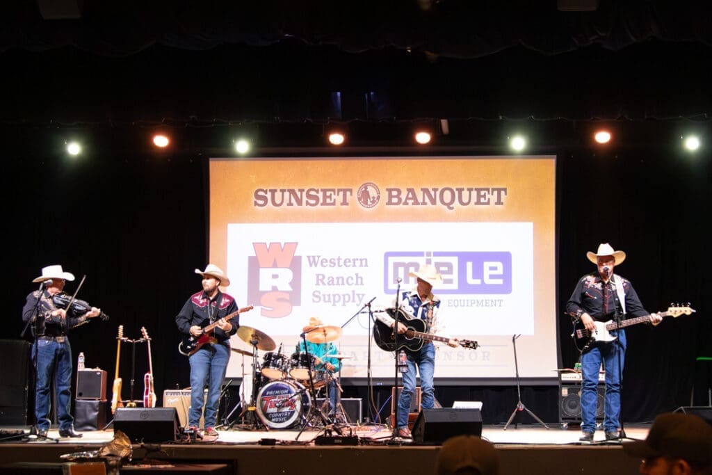 Five-member country band wearing cowboy hats performs on stage with a drummer behind and a Sunset Banquet banner in the background.