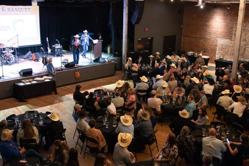 A country-themed banquet with a live band on stage and guests in cowboy hats seated at round tables watching the performance.